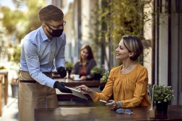 Masked server talks with female diner at outdoor restaurant