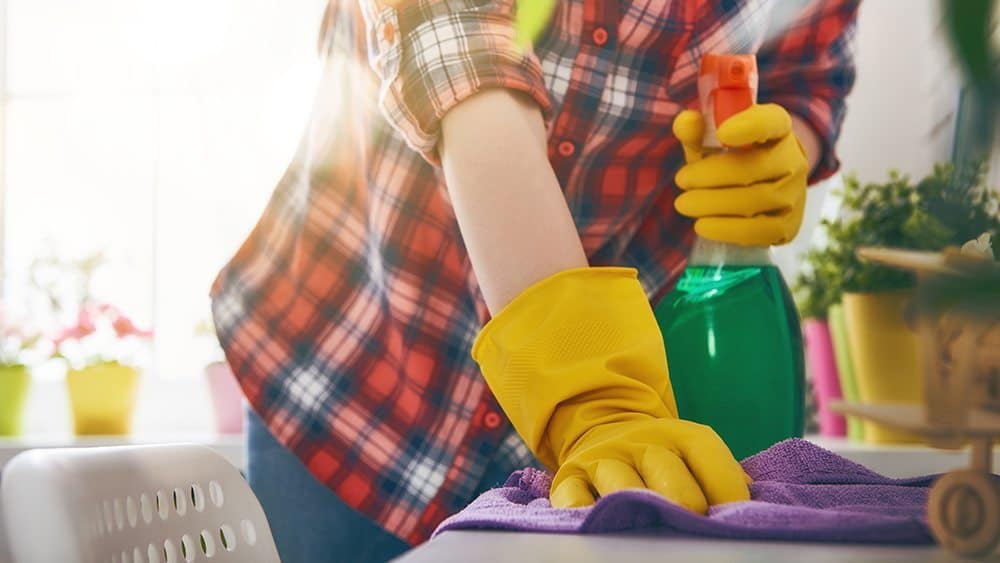 Person cleaning table with cloth and cleaner spray